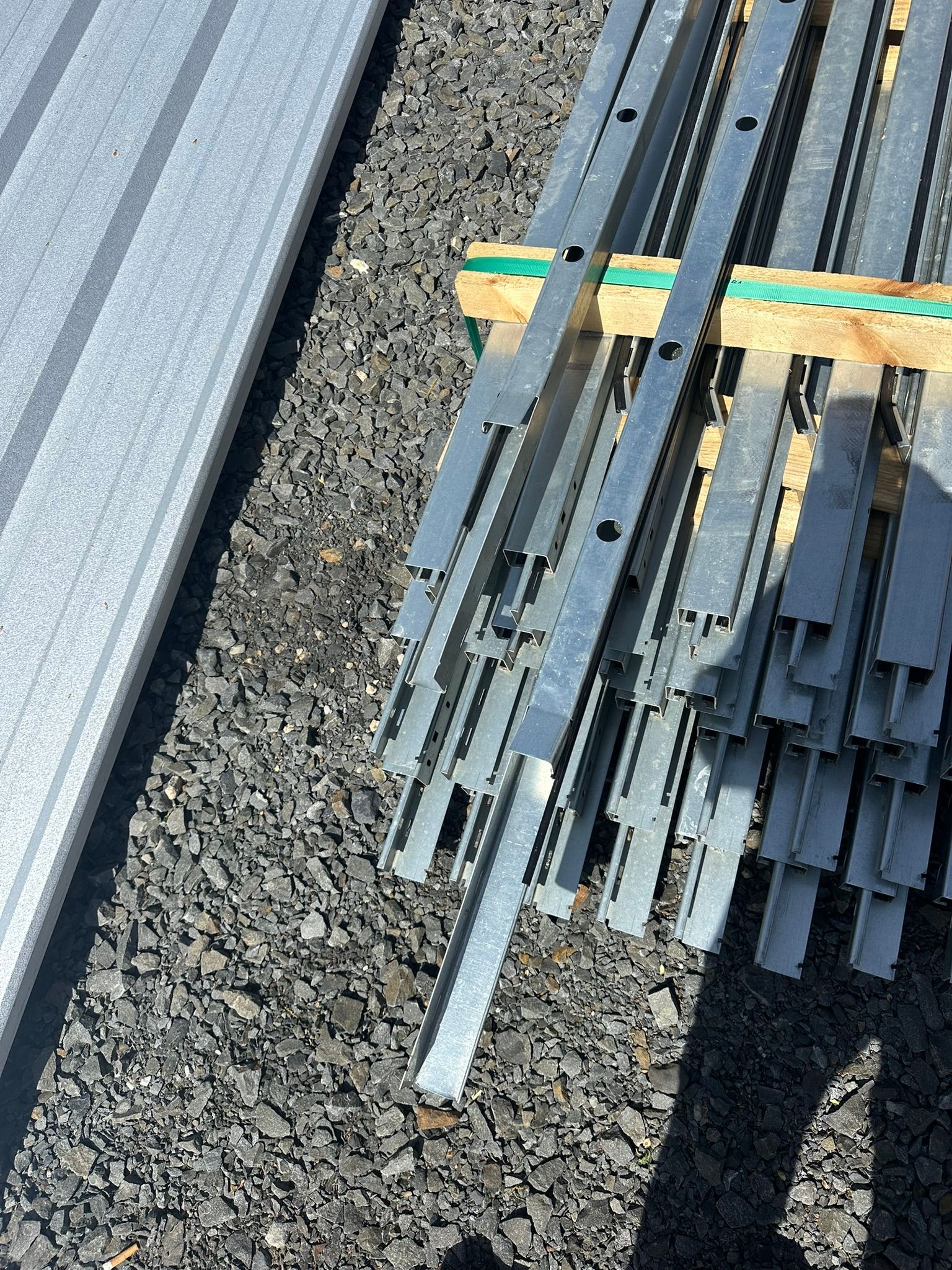 Stack of gray metal rods on gravel beside a corrugated roof edge