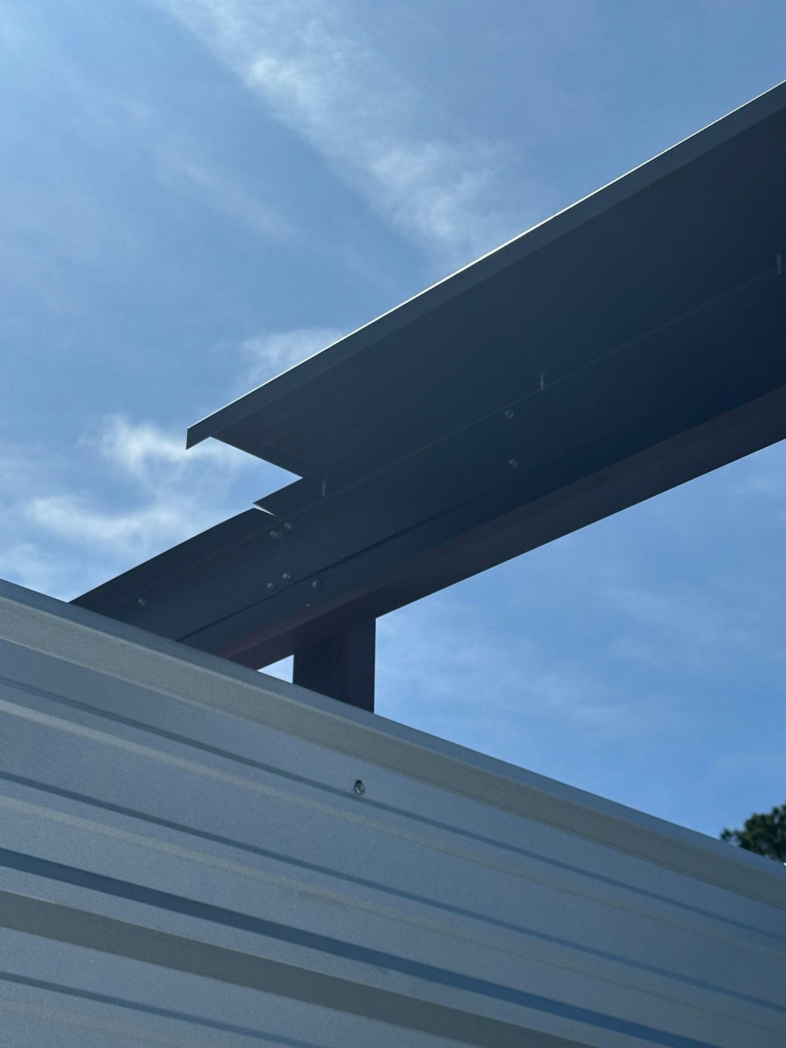 Blue sky above a corrugated metal roof and dark steel beams outdoors