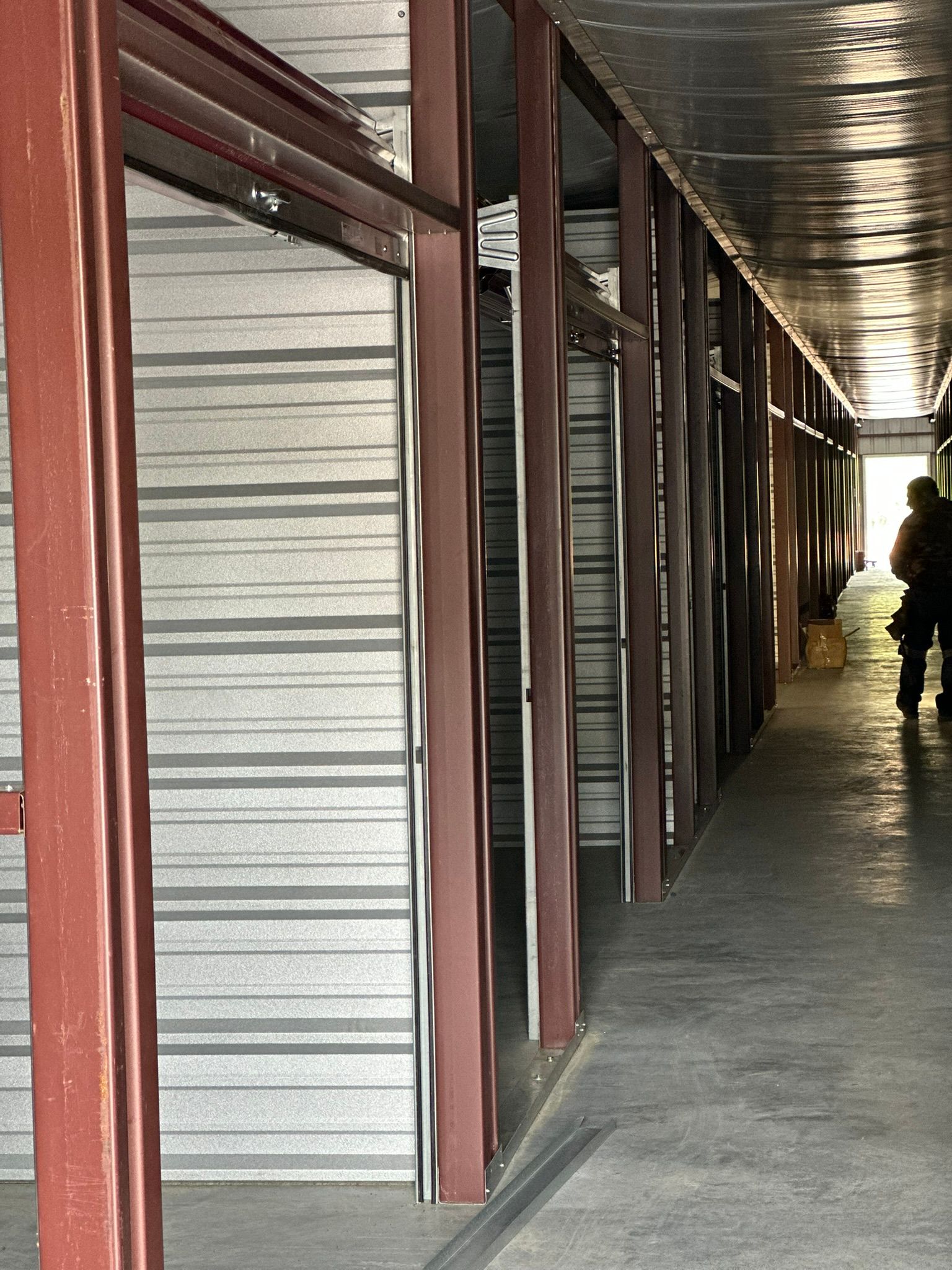 Long corridor with red posts and a row of gray metal storage units, with a person in the distance