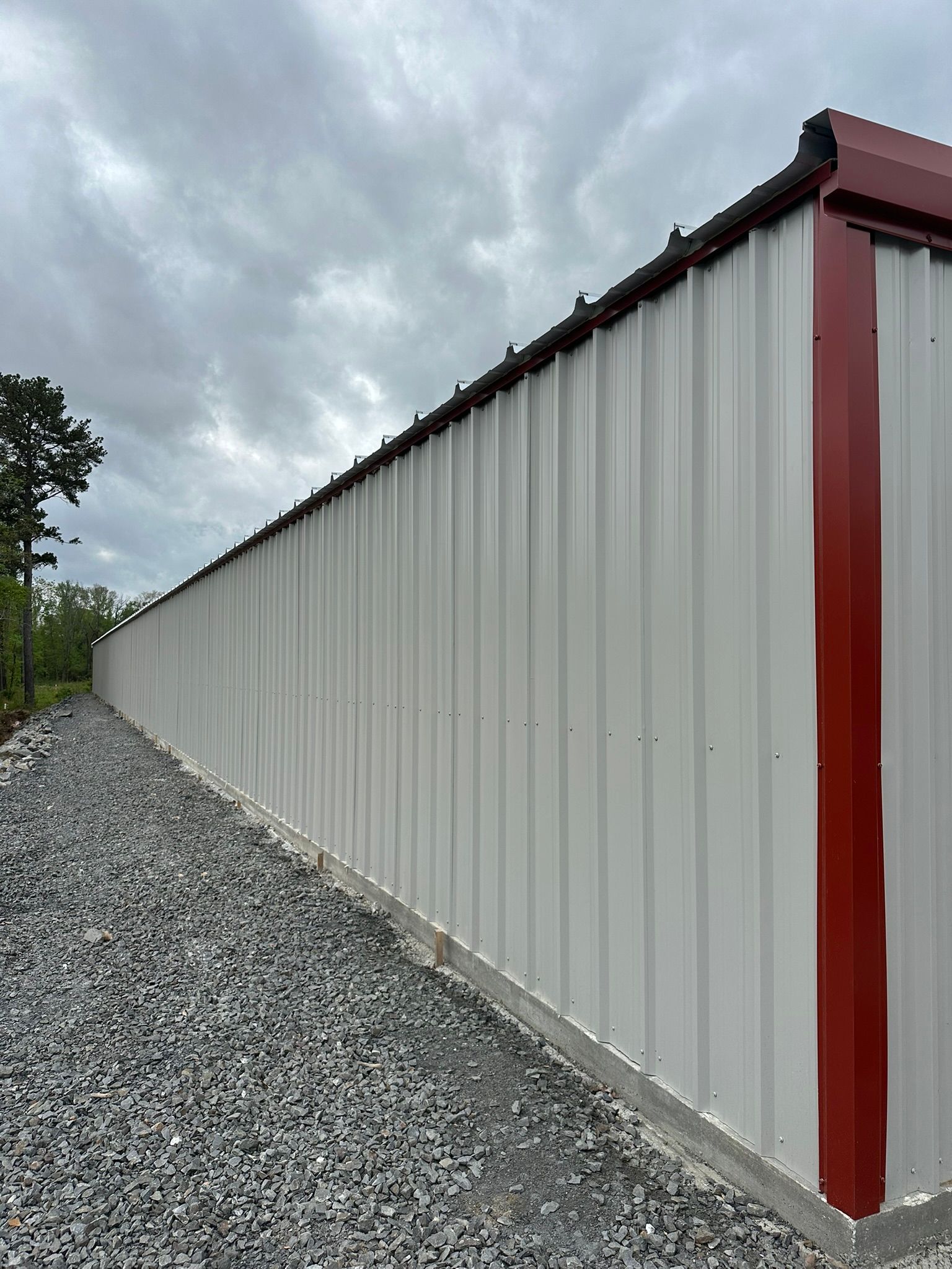 Long white metal building with red trim beside a gravel path under a cloudy sky