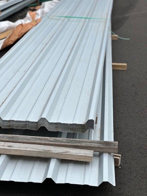 Stacked white corrugated metal roofing sheets on pallets outdoors