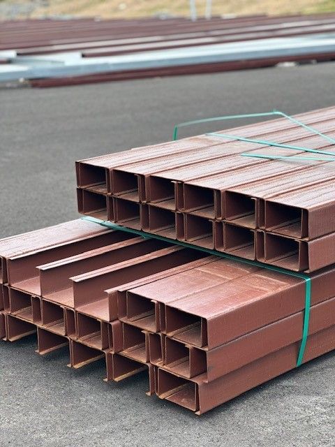 Stacked copper-colored metal pipes bundled with green straps on a pavement.