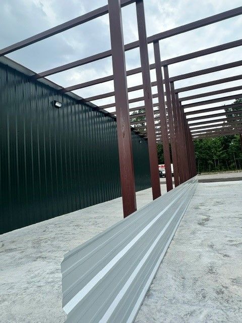 Covered walkway with red steel posts, green wall, and metal roof frame over gravel ground
