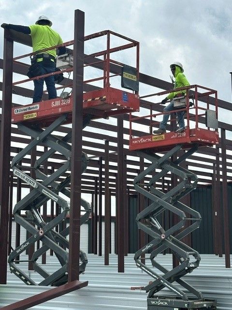 Workers on red scissor lifts installing metal beams at a construction site