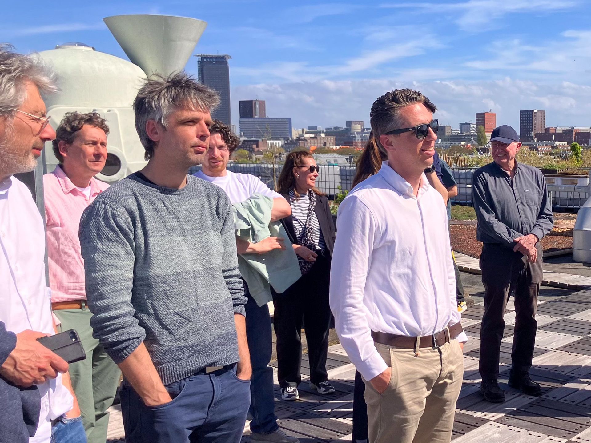 Mensen staan ​​buiten op een dak en luisteren naar een luidspreker met de skyline van de stad op de achtergrond.