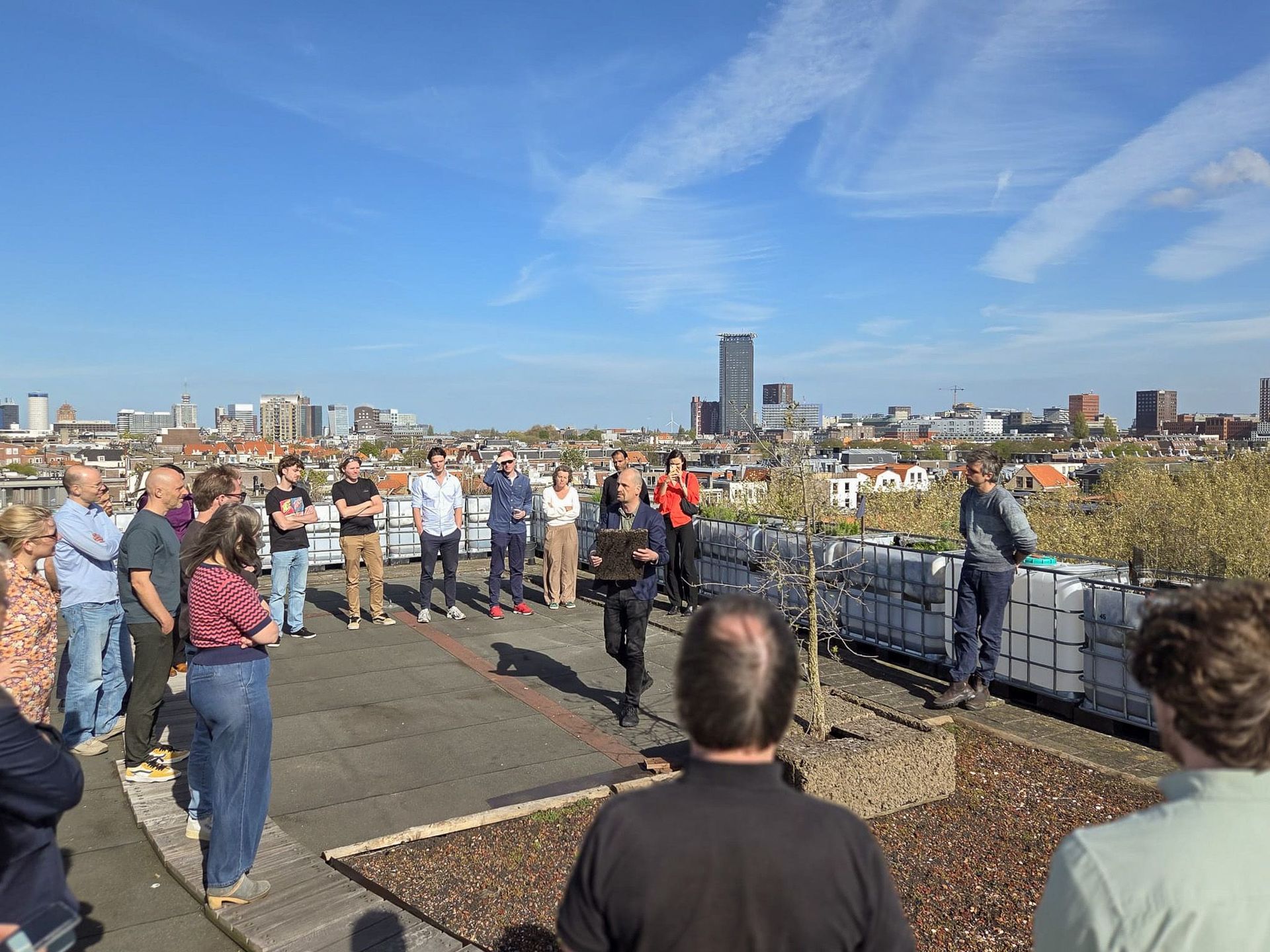 Mensen hadden zich verzameld op een dakterras met uitzicht op de skyline van de stad onder een blauwe hemel.