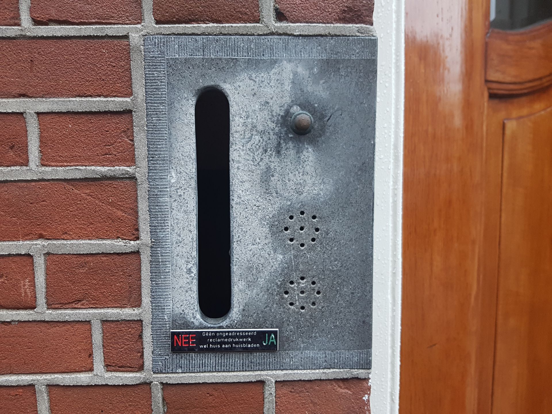 Brievenbus en intercom in een rode bakstenen muur naast een houten deur.