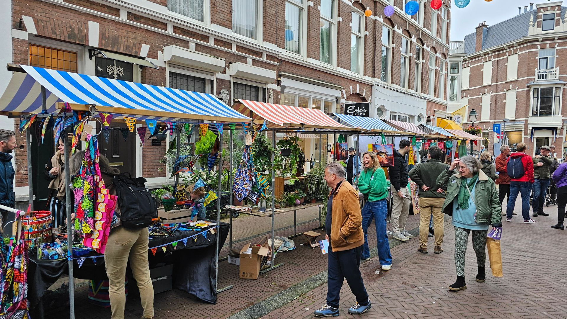 Straatmarktstalletjes met kleurrijke koopwaar en winkelend publiek op een met bakstenen bestrate stadsstraat