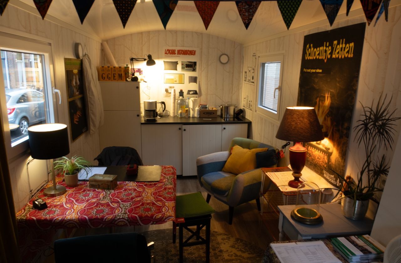 Gezellig, licht interieur van een kleine hut met kleurrijke decoraties, een kleine keuken, een fauteuil, een tafel en een bureau.
