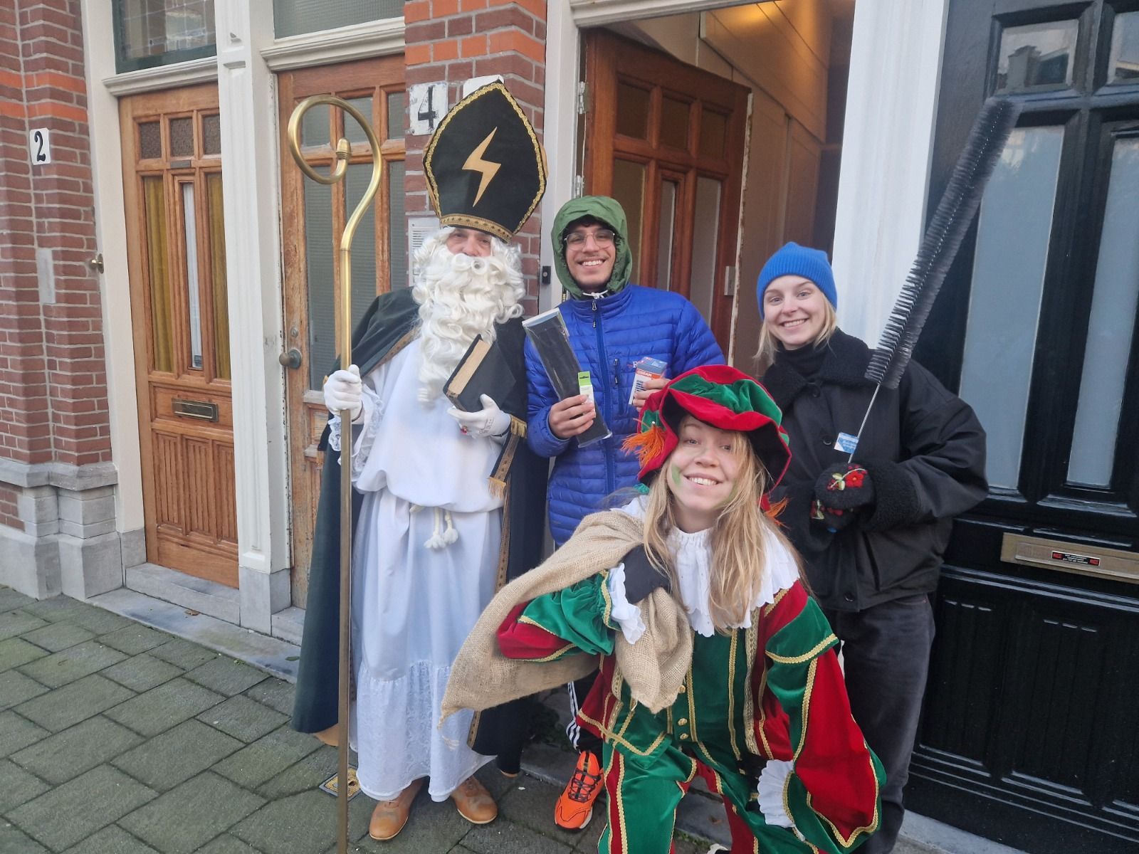 Sinterklaas en twee Pieten poseren met twee mensen voor een gebouw.