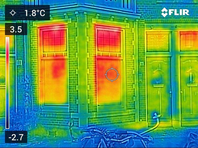 Thermische afbeelding van de buitenkant van een gebouw, waarop warmteverlies via ramen en deuren in rode en gele tinten te zien is.