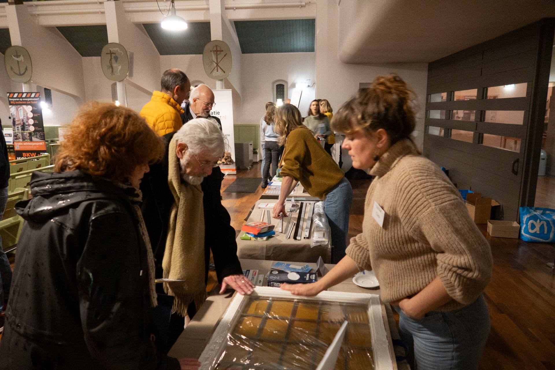 Mensen bekijken kunstwerken die tentoongesteld worden tijdens een evenement binnenshuis; een vrouw gebaart naar het kunstwerk.