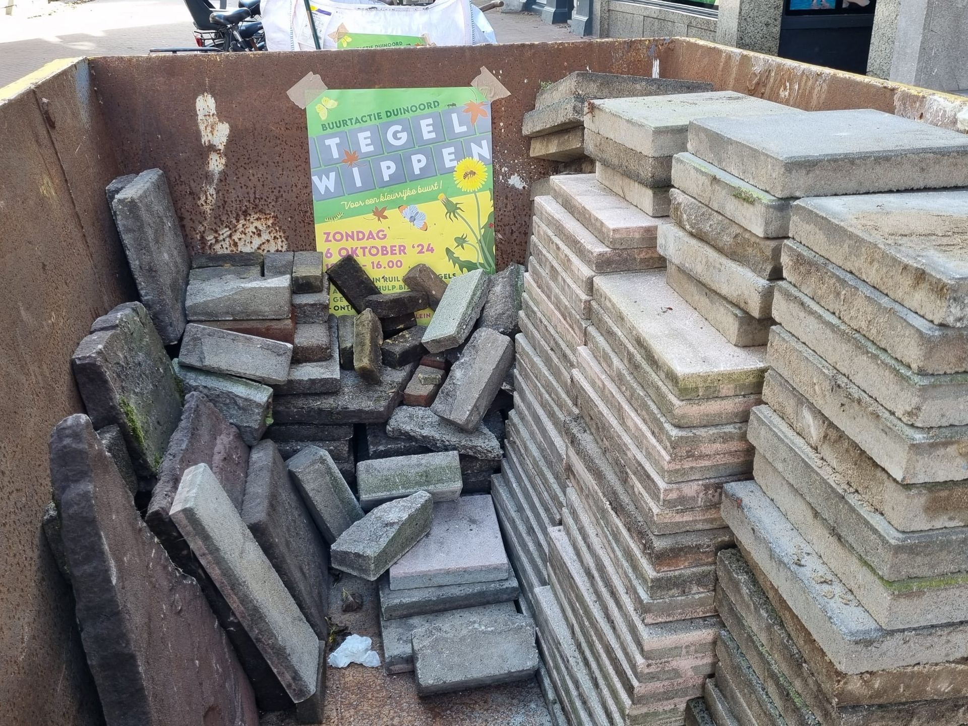 Metalen container gevuld met betontegels en een poster.