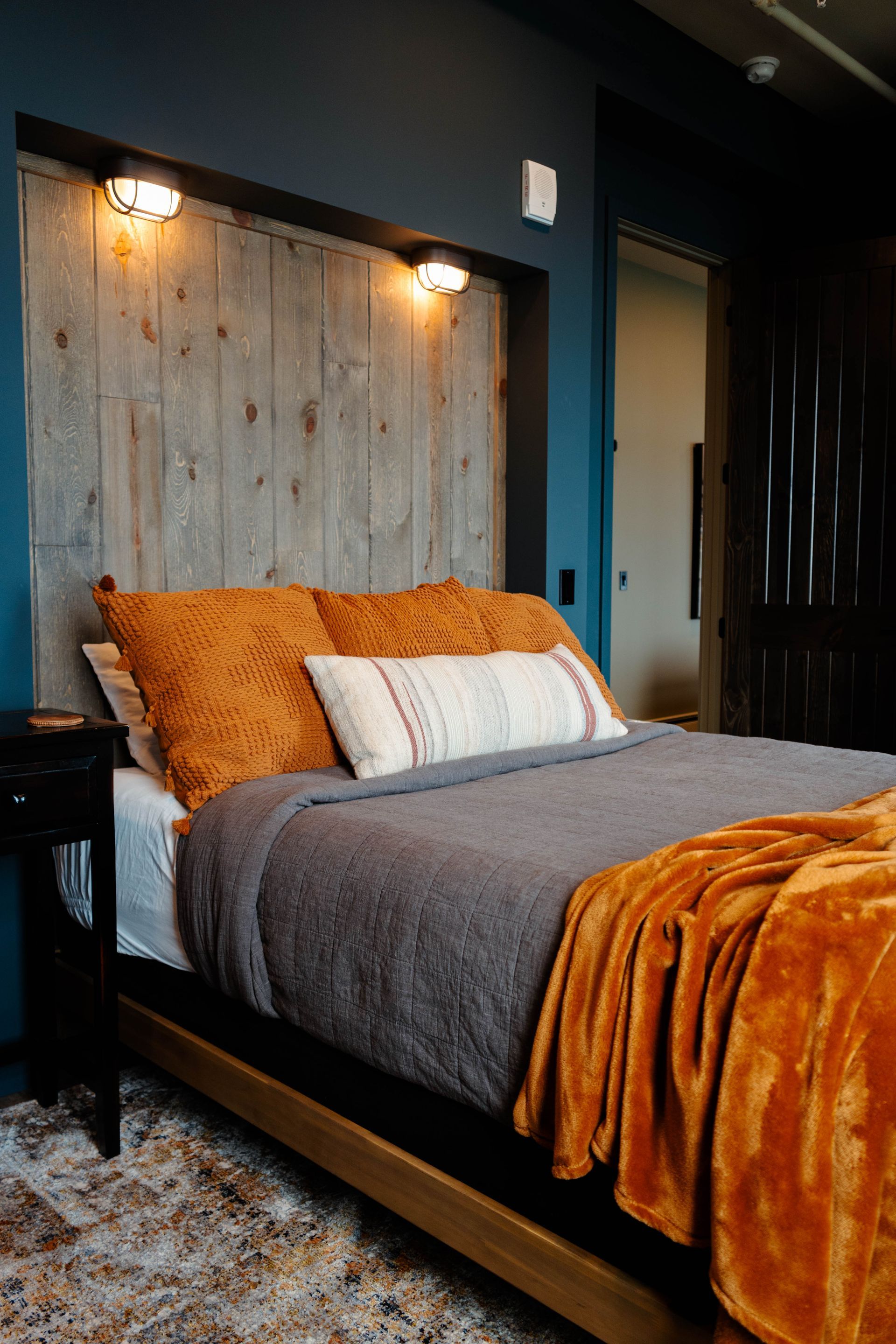 Cozy bedroom with a black bedframe, gray bedding, mustard throw, and rustic wood accent wall with lights