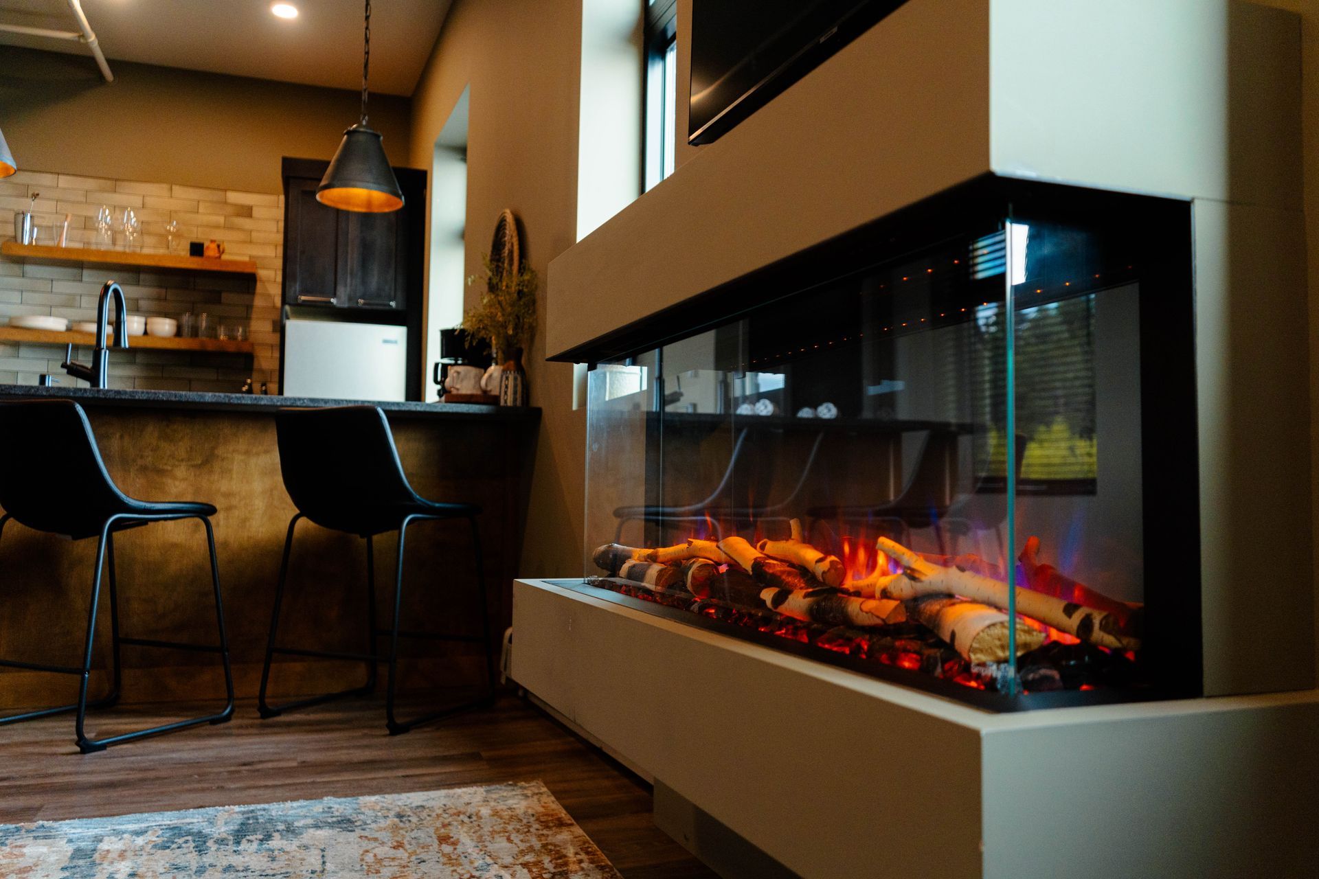 Modern living room with a glass fireplace, bar stools, and warm amber lighting