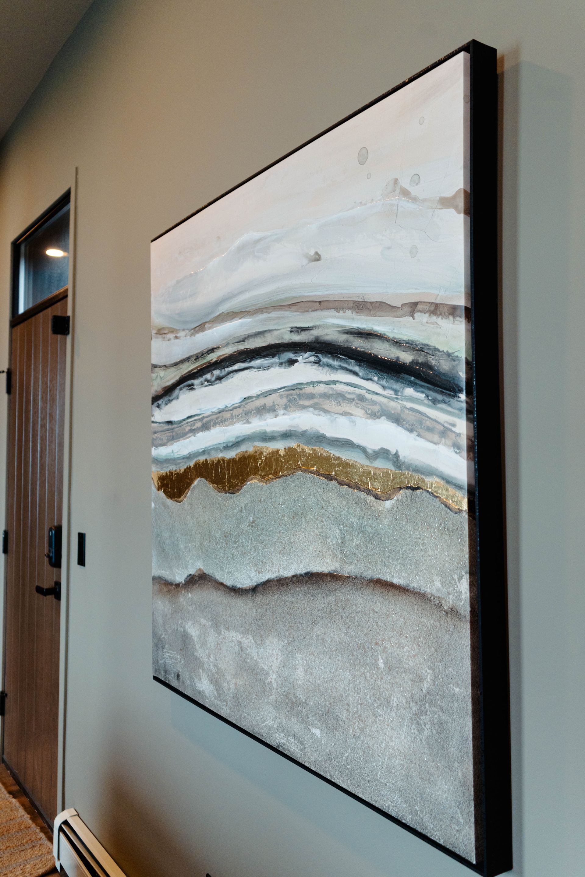 Framed abstract wall art with gray, white, black, and gold waves in a hallway