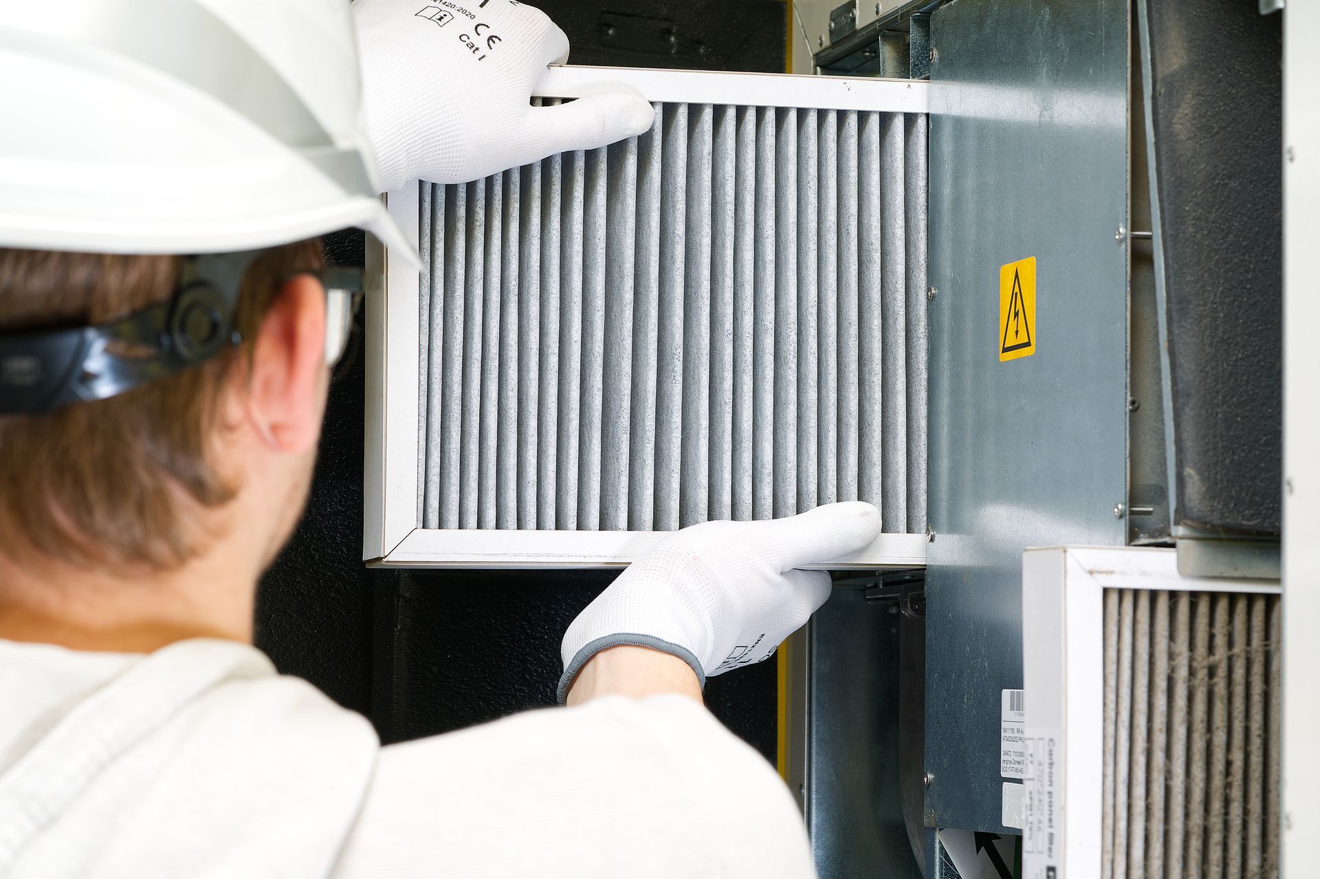 Technician in white gloves and hard hat inspecting industrial filter unit inside machinery cabinet