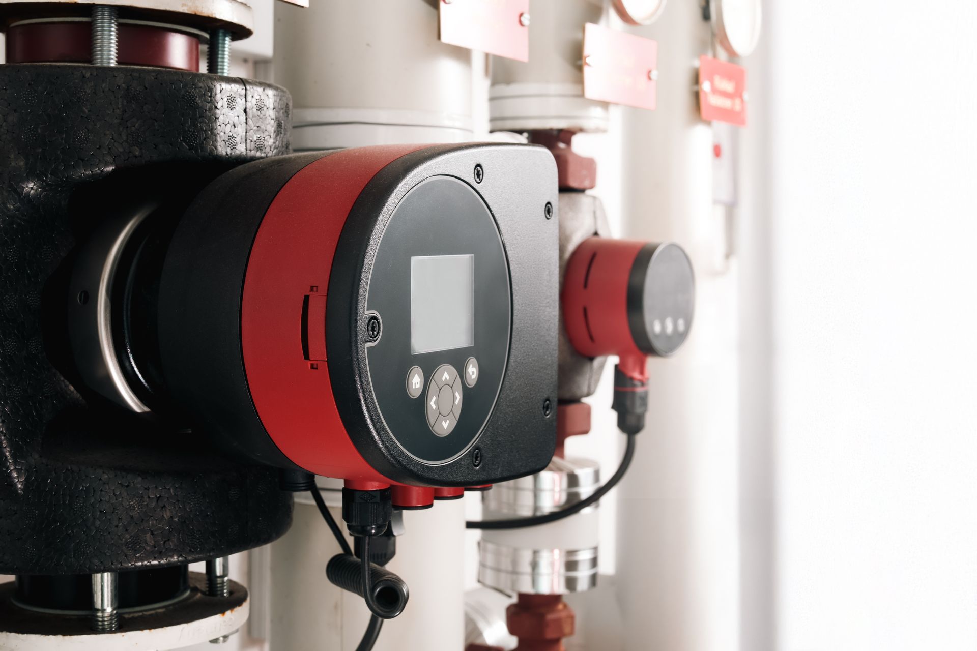 Red and black industrial control units mounted on metal pipes in a utility room