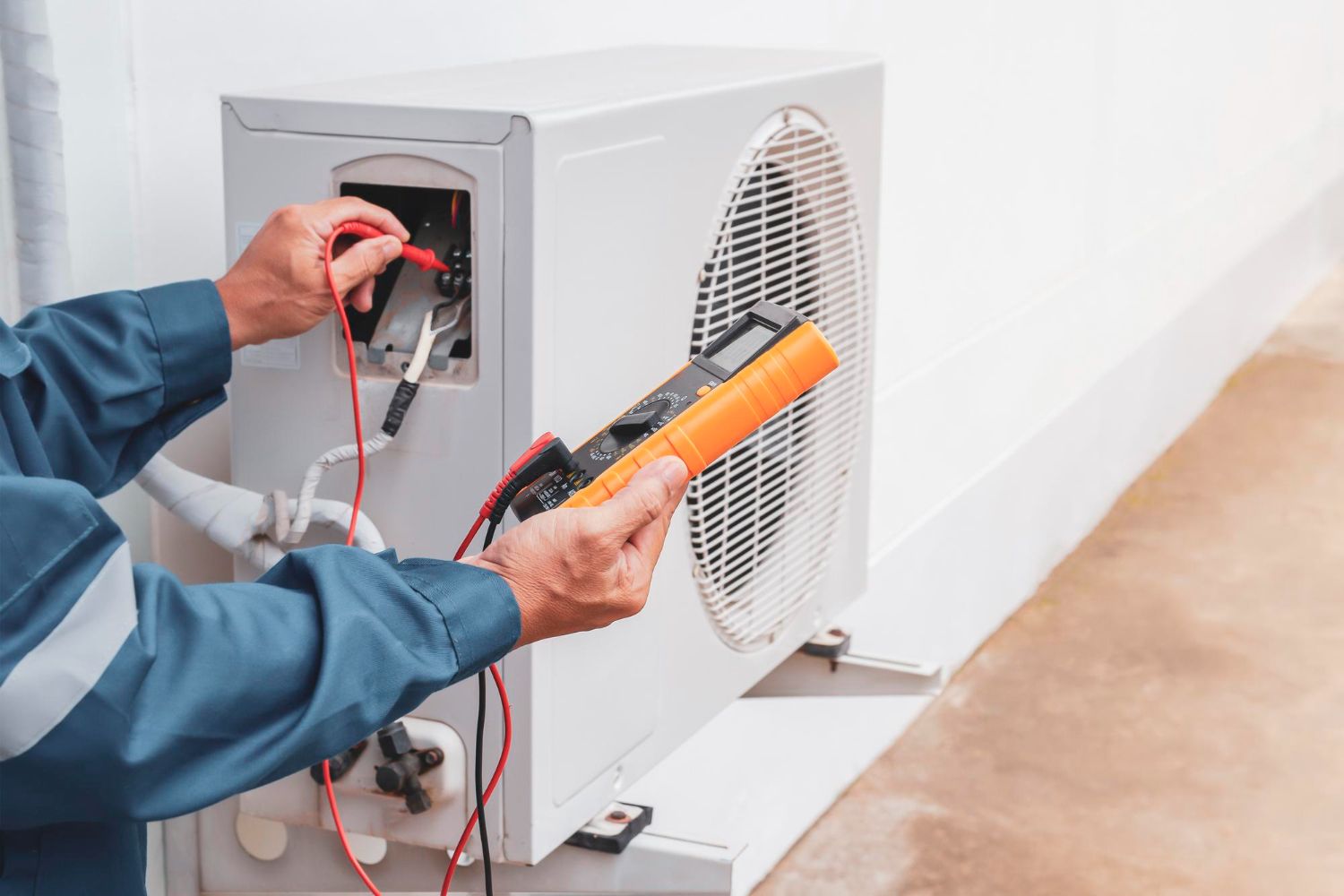 Person in blue coveralls using a multimeter to test an outdoor AC unit.