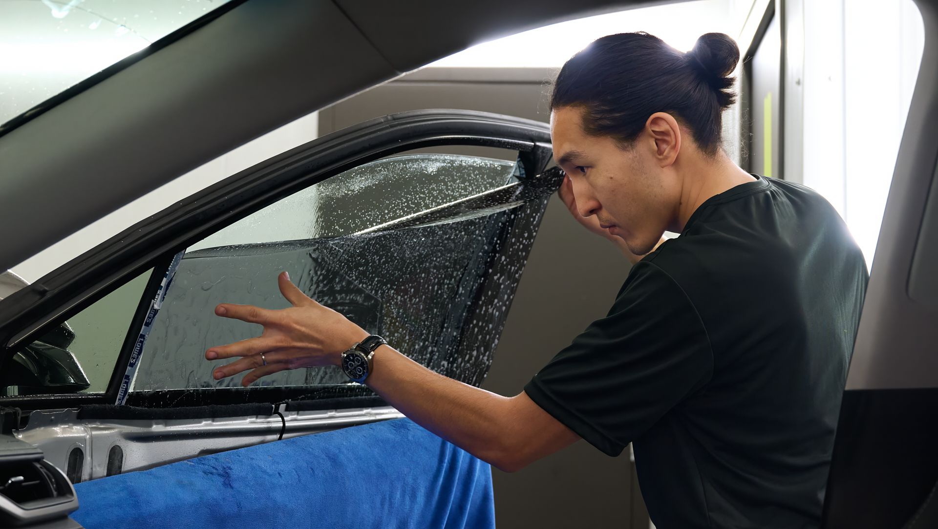 A man is applying window tinting to a car window.