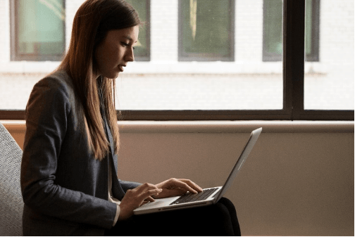 A woman is sitting in front of a window using a laptop computer.
