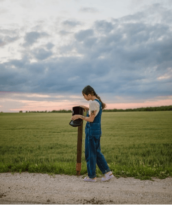 A woman is standing next to a mailbox in a field.