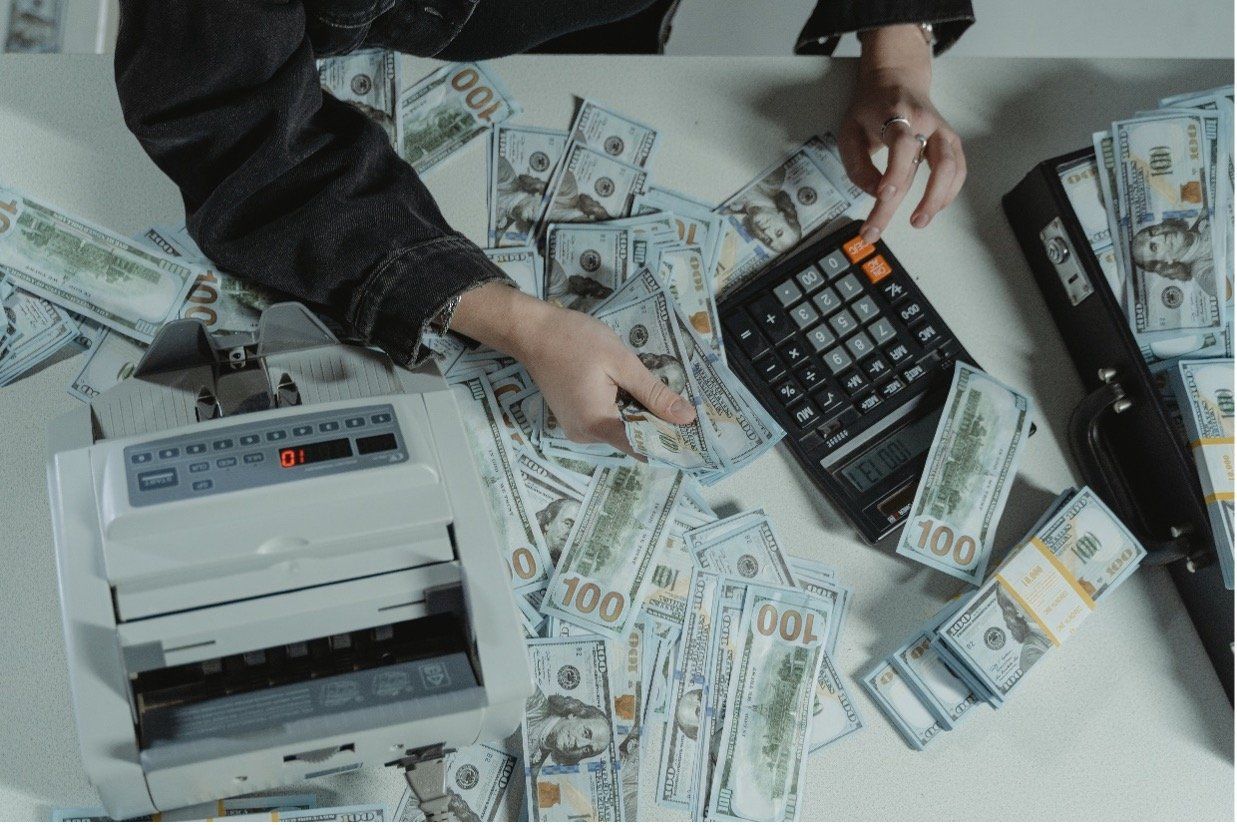 A person is sitting at a table with a pile of money and a calculator.