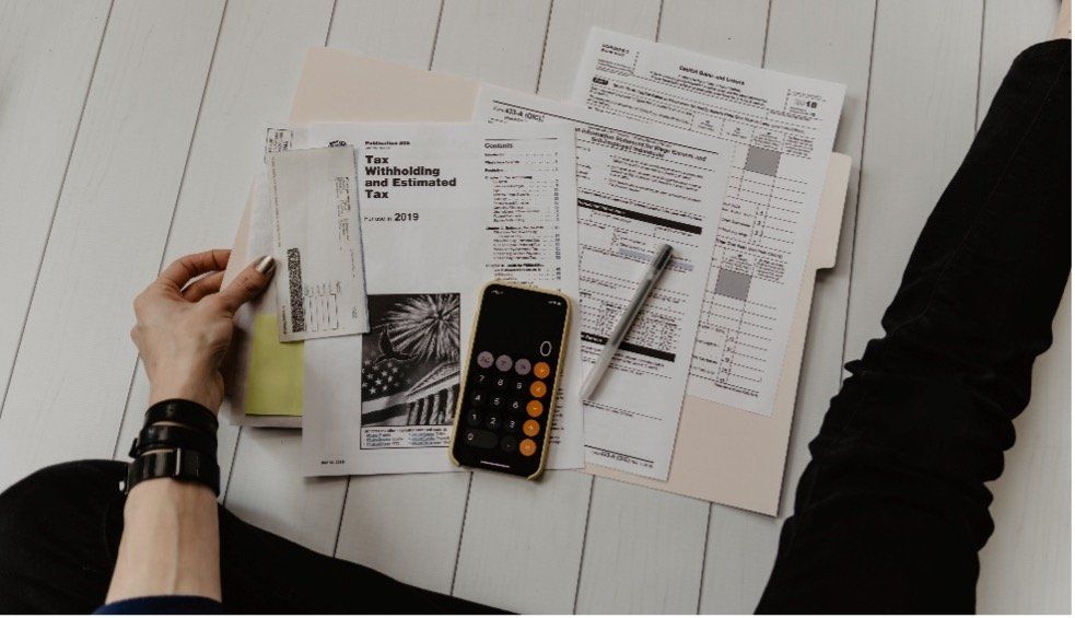 A person is sitting on the floor with papers and a calculator.