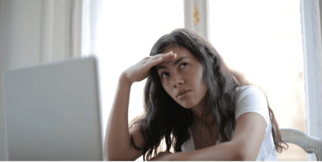 A woman is sitting in front of a laptop computer with her hand on her forehead.