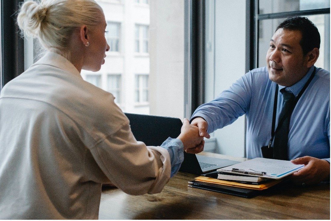 A man and a woman are shaking hands at a table.