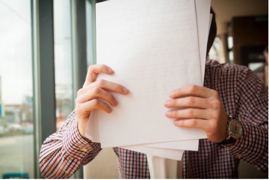 A man is holding a stack of papers in front of his face.