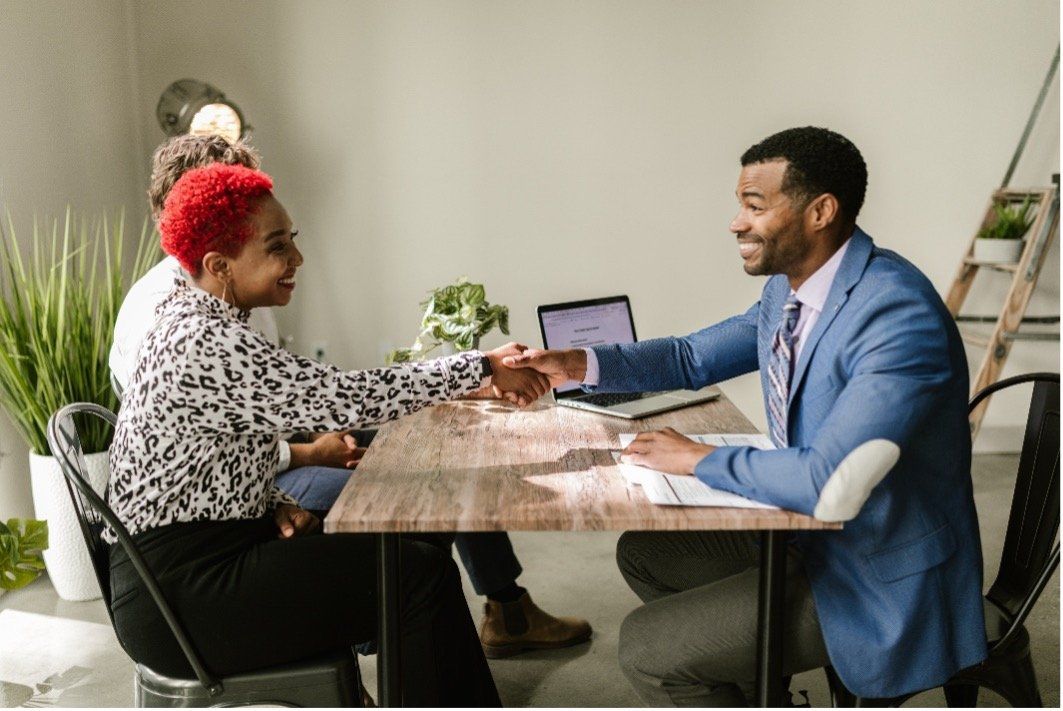 A man and a woman are shaking hands at a table.