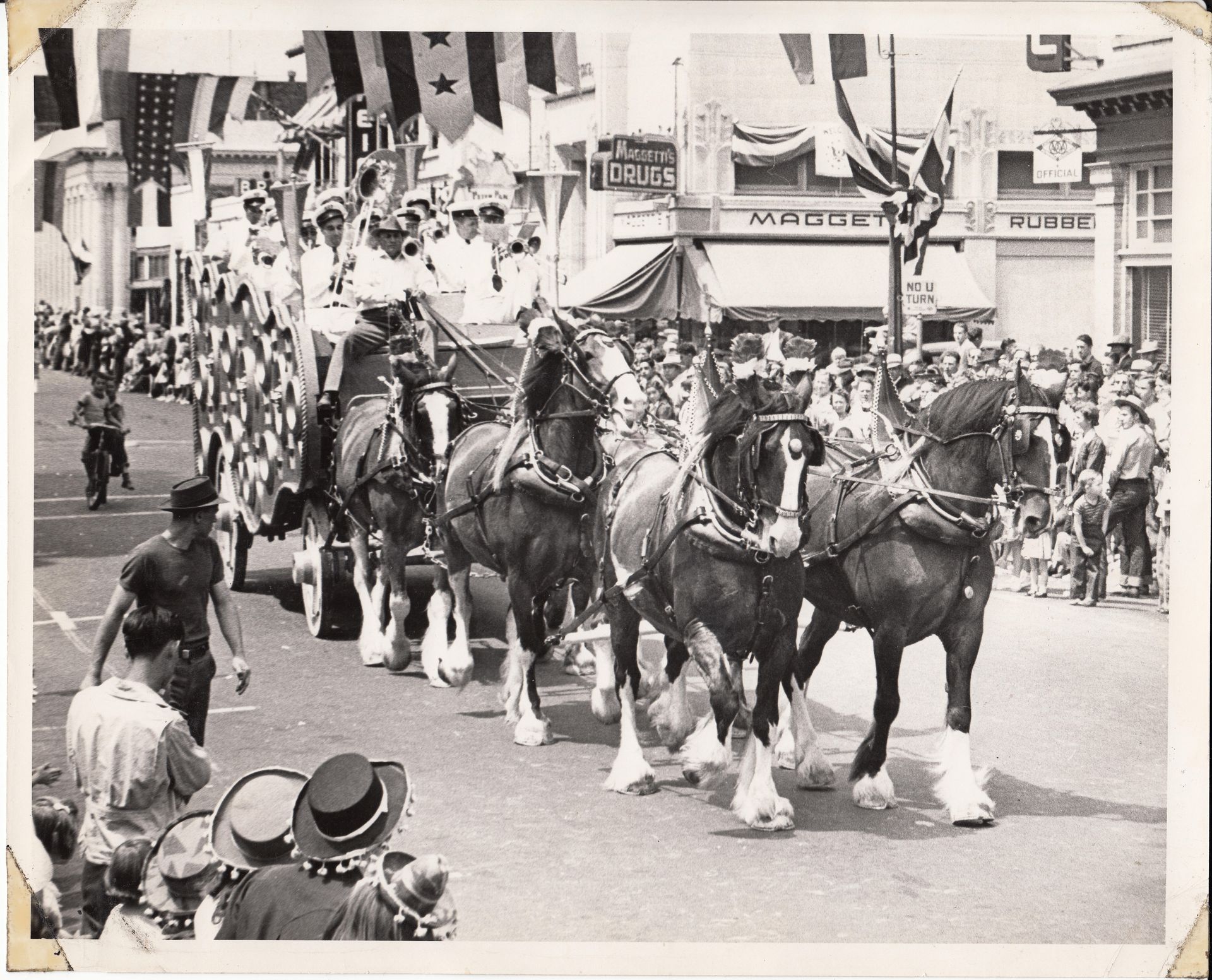 Horse-drawn parade with riders and spectators lining a street in a bustling town.