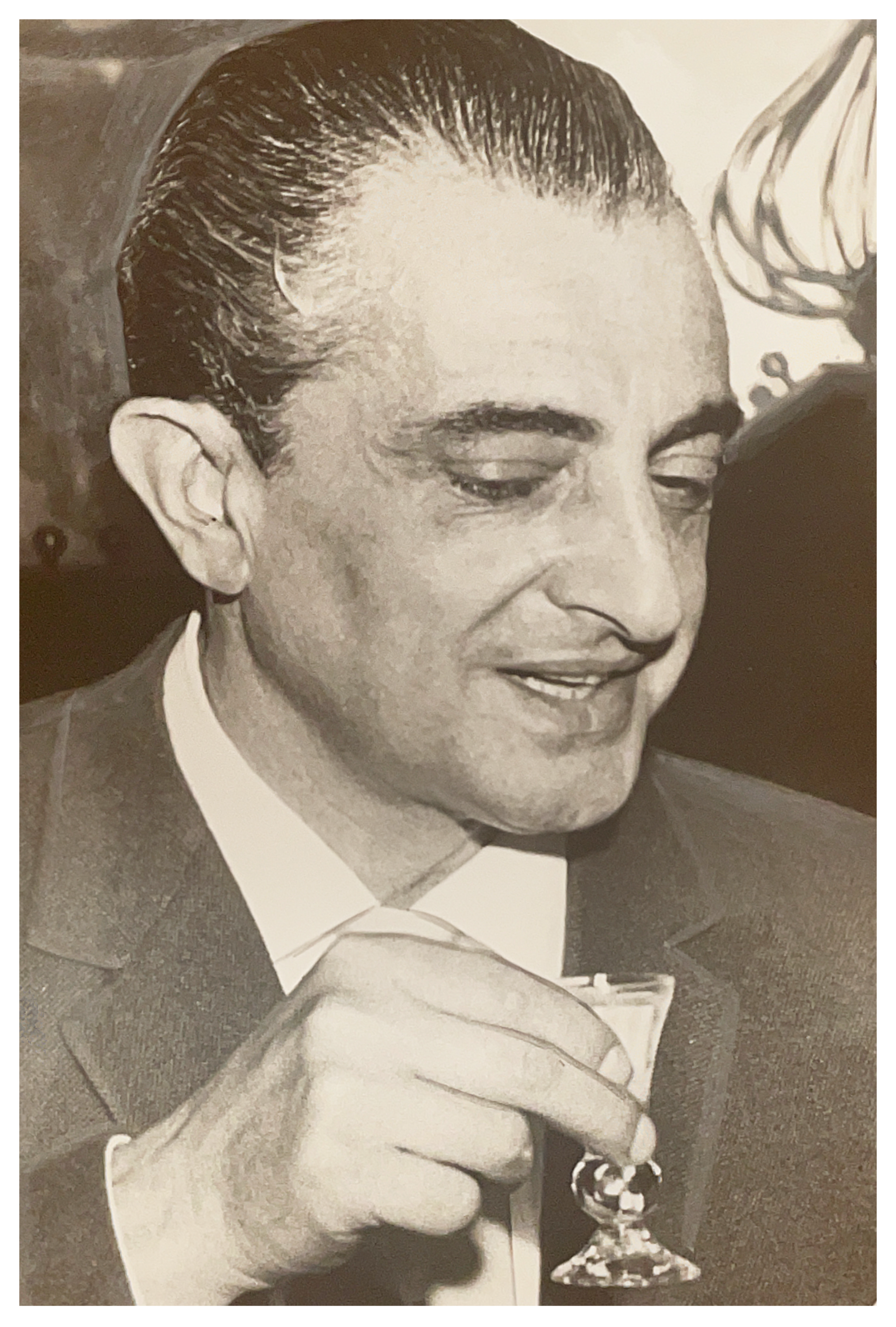 Alexis Merab in a suit smiling and holding a wine glass at a formal event