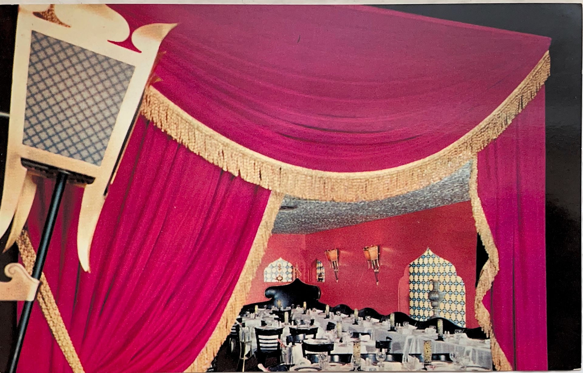 Pink draped stage curtains with gold trim framing a small cityscape set and arched window backdrop