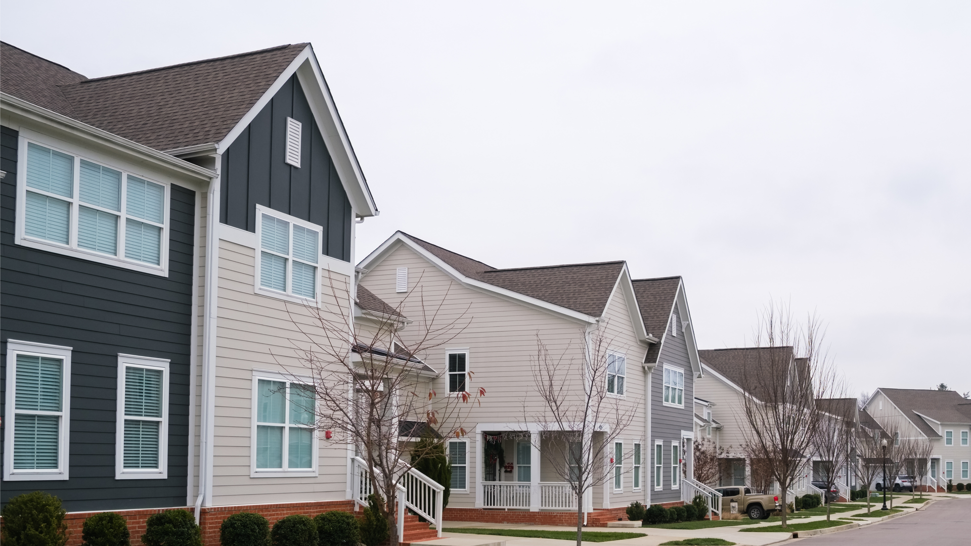 Row of modern suburban townhouses with gray and white siding along a quiet street