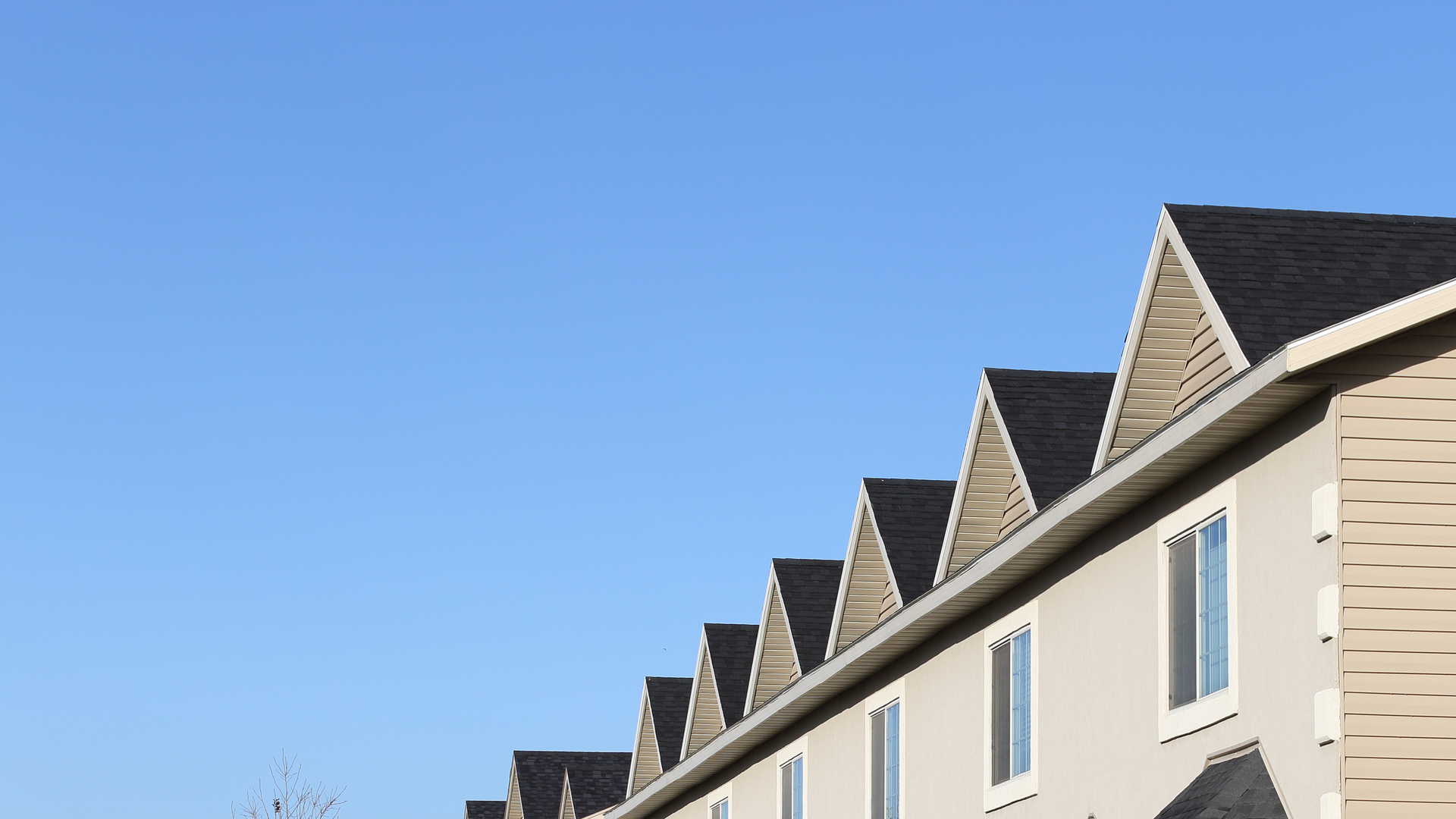Row of beige townhouses with dark roofs against a clear blue sky