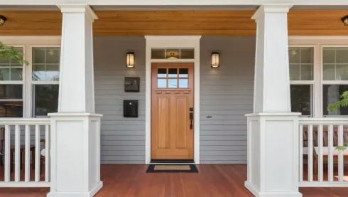 Front porch with a wooden front door, white columns, and gray siding on a house
