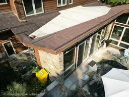 Aerial view of a house roof with a new white roof section beside an older brown roof and stone chimney.