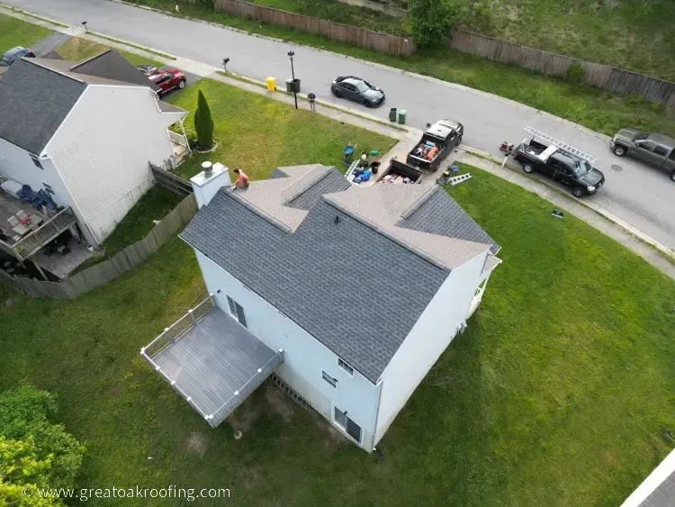 Aerial view of a white house with a gray roof and solar panels, parked cars along the road nearby.