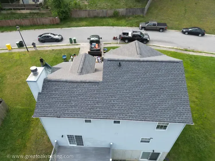 Aerial view of a white house with a gray roof, parked cars, and a street beside a grassy yard.