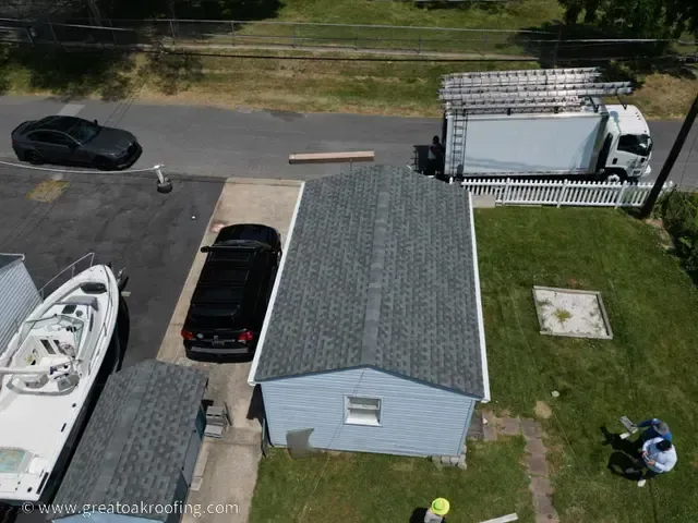 Aerial view of a small blue shed, parked vehicles, and a white truck by a roadside yard