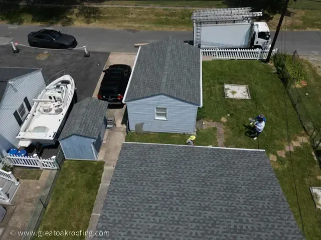 Aerial view of a house with a driveway, parked boat, shed, and grassy yard next to a road.