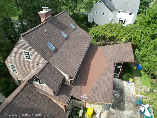 Aerial view of a brown house with a steep roof, skylights, and an attached covered patio beside a driveway.