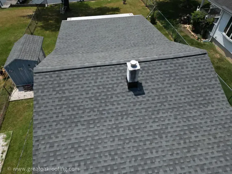 Aerial view of a gray shingled house roof with a chimney and a small shed beside it.