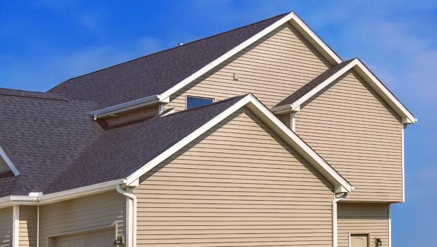 Beige house with dark gray shingled roof and blue sky above