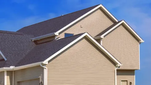 Beige house with dark gray shingled roof and blue sky above