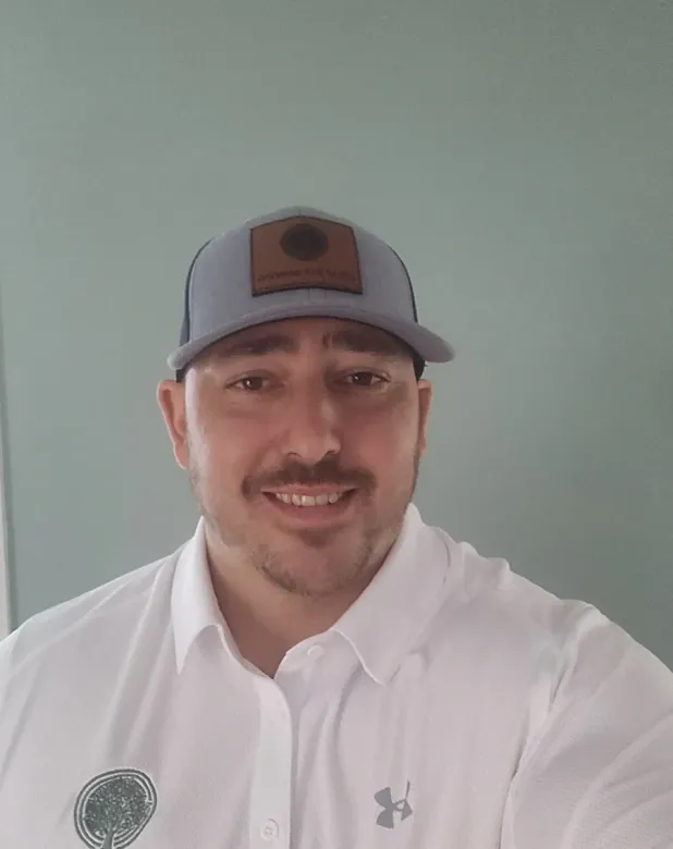 Smiling man in a gray cap and white shirt posing against a plain green wall