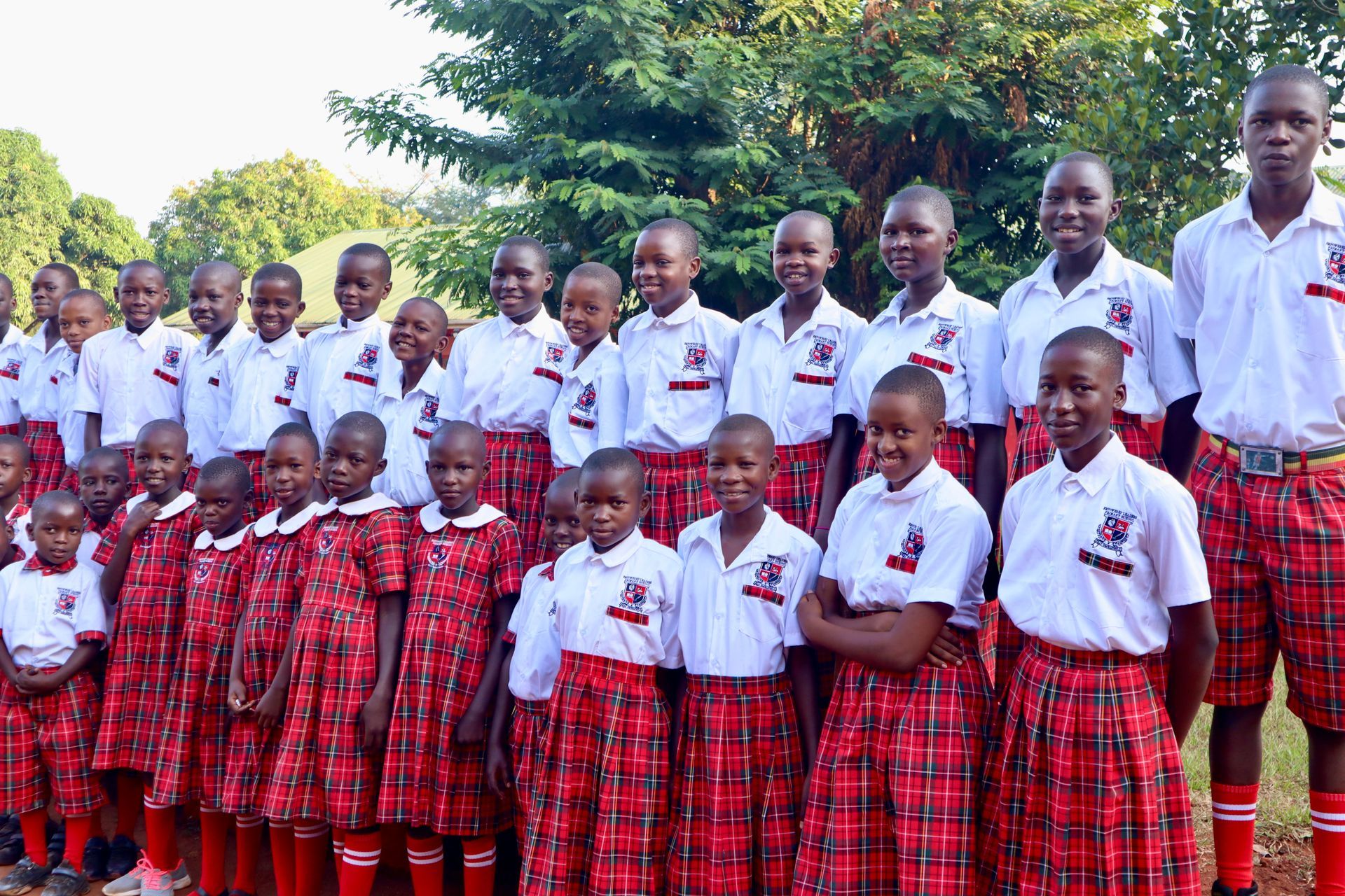 Group of African school children in red and white uniforms, posing outdoors.