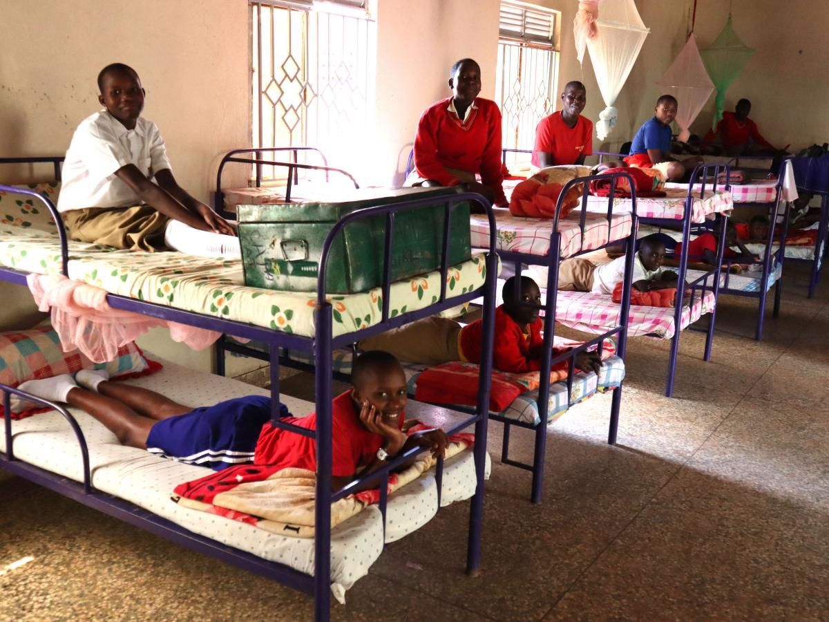 Children in a school dormitory; bunk beds; some kids sit or lie on beds, others stand.